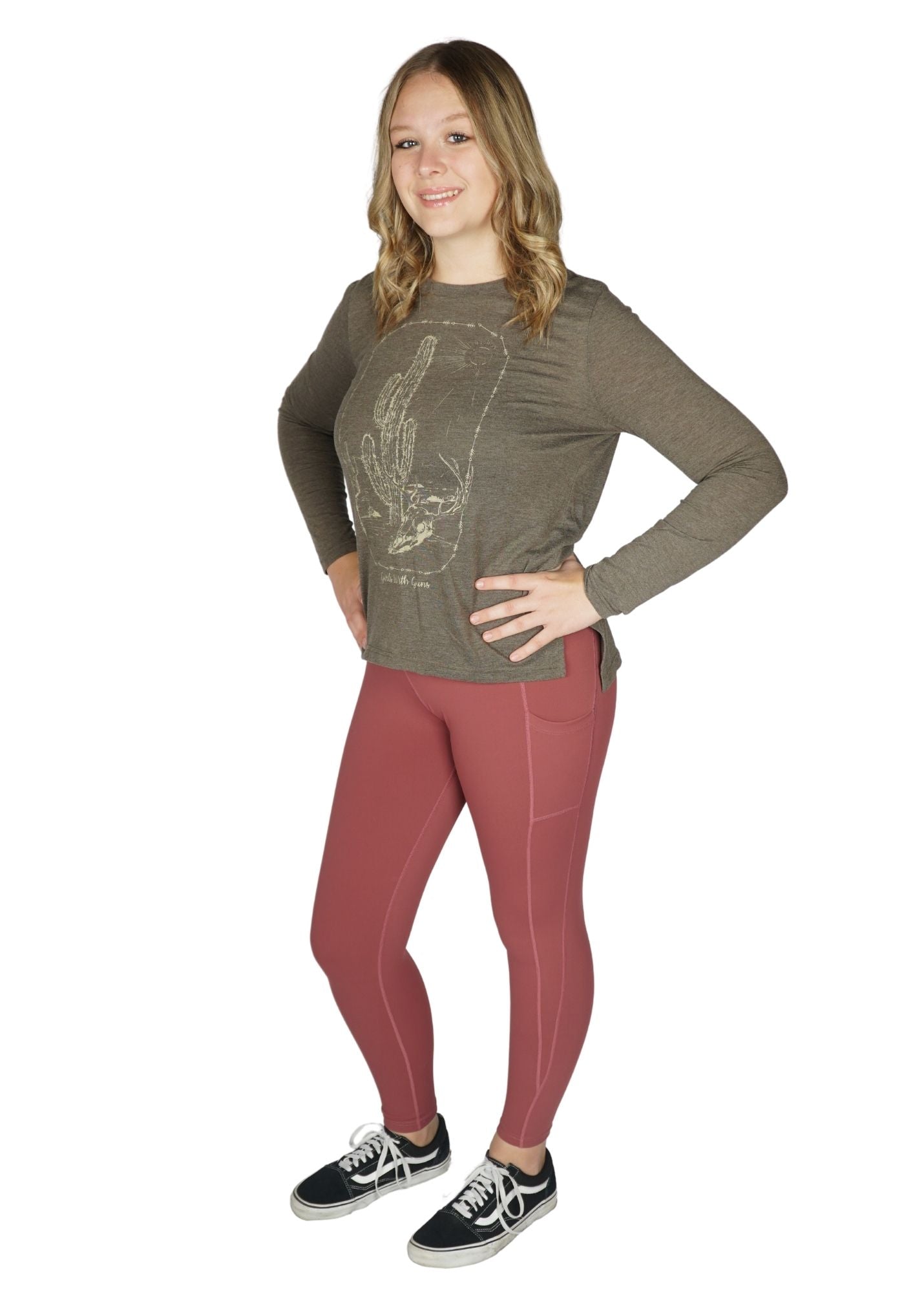 A woman standing and posing in mauve colored leggings and a green top with a graphic design.