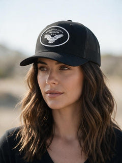 A lady wearing a black trucker hat with an eagle landing and the words Girls with Guns and FREEDOM