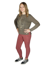 A woman standing and posing in mauve colored leggings and a green top with a graphic design.